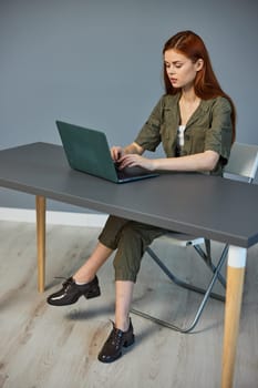 photo of a woman sitting at a table with a laptop in the office against the background of a blue wall. High quality photo