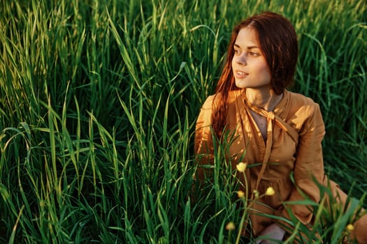 a happy woman lies in the tall green grass in a long orange dress and looks away smiling pleasantly. High quality photo
