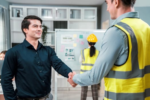 An engineer with a protective vest handshake with an investor in his office. Following a successful meeting, employee and employer form a partnership.