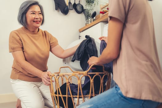 Daughter and mother working together to complete their household chores near the washing machine in a happy and contented manner. Mother and daughter doing the usual tasks in the house.