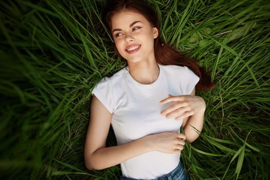 a portrait of a laughing woman with healthy, even teeth lies in the green grass. High quality photo