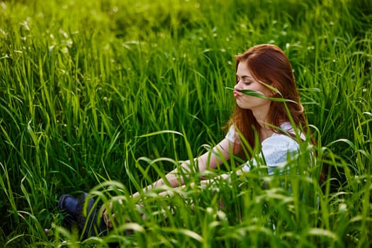 funny woman sits in high grass making herself a mustache from a blade of grass. High quality photo