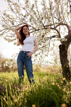 joyful, happy woman in jeans and a light T-shirt posing against the backdrop of a flowering tree. High quality photo