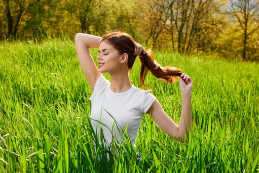 beautiful woman sitting in tall grass adjusting her hair. High quality photo