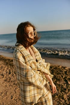 a woman in large glasses wrapped in a plaid enjoys the view of the setting sun standing on the beach. High quality photo