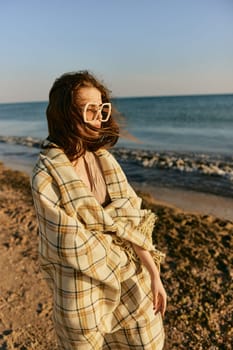 a woman in large glasses wrapped in a plaid enjoys the view of the setting sun standing on the beach. High quality photo