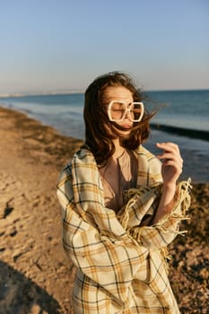 portrait of a woman in a blanket standing on the shore and straightening her hair flying in the wind. High quality photo