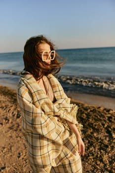 a woman in large glasses wrapped in a plaid enjoys the view of the setting sun standing on the beach. High quality photo