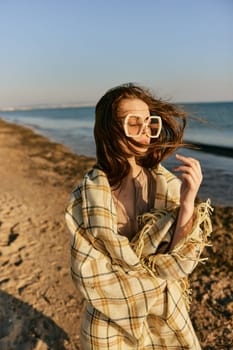 portrait of a woman in a blanket standing on the shore and straightening her hair flying in the wind. High quality photo