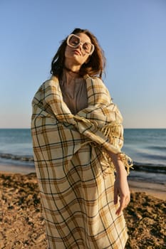 a cute woman stands with a plaid during sunset on the beach and the wind blows her red hair. High quality photo