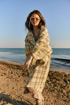 a woman wrapped in a plaid stands on the seashore in bright sunglasses and squints from the sun. High quality photo