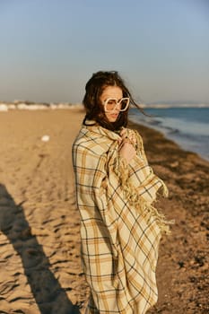 a beautiful woman wrapped in a plaid stands on the seashore against the backdrop of sunset. High quality photo