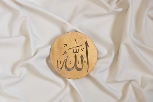 Allah bismillah names . Golden wooden calligraphy of islam god. on white textile, top view