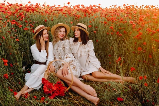 Funny girls in dresses and hats in a poppy field at sunset.