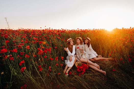 Funny girls in dresses and hats in a poppy field at sunset.