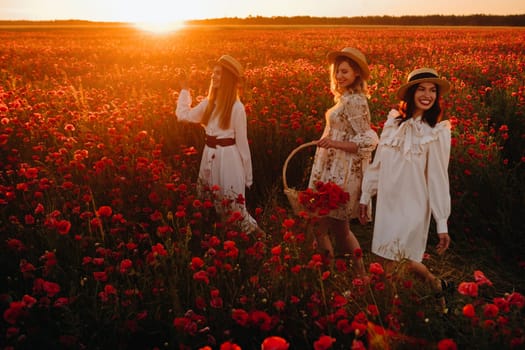 Funny girls in dresses and hats in a poppy field at sunset.