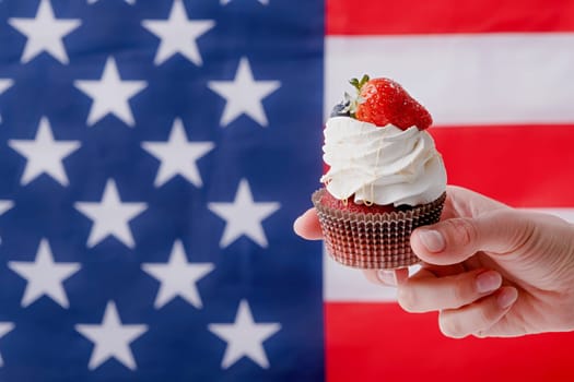 Fourth of july celebration. hand holding sweet cupcake with blueberries and strawberry , flag background