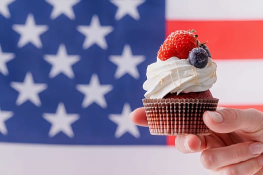 Fourth of july celebration. hand holding sweet cupcake with blueberries and strawberry , flag background