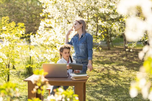 Woman and little girl laying on the spring flower field outdoors - having fun using a laptop