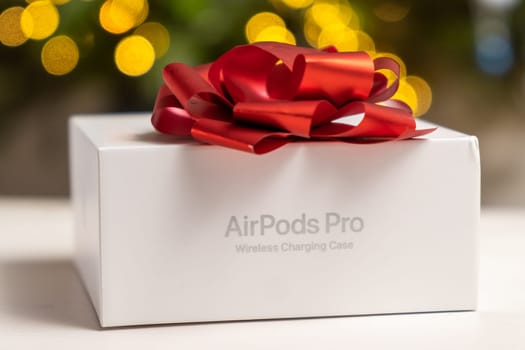 AirPods Pro box with a red bow against a blurred background. Gifts from Apple for Christmas or New Year parties, October 2022, Prague, Czech Republic.