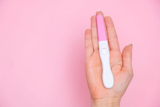 Female hand holding a negative pregnancy test on the pink background with copy space.