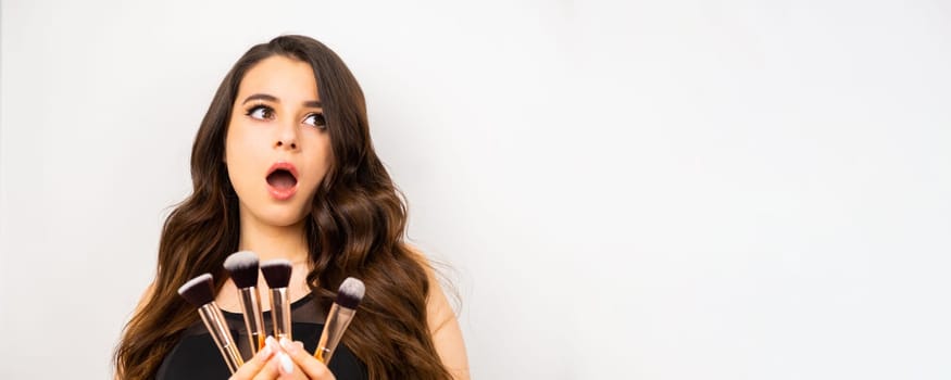 Banner with an attractive excited woman holding a set of makeup brushes for professional use, copy space.