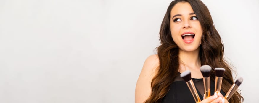 Beauty portrait of a joyful woman holding makeup brushes on a white background, banner