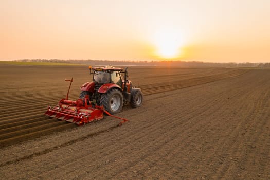 PRAGUE , CZECH REPUBLIC - MARCH 18 2022: Modern tractor cultivates soil in field on agricultural farm at bright sunset. Powerful machine works dragging plow behind at rural site in evening