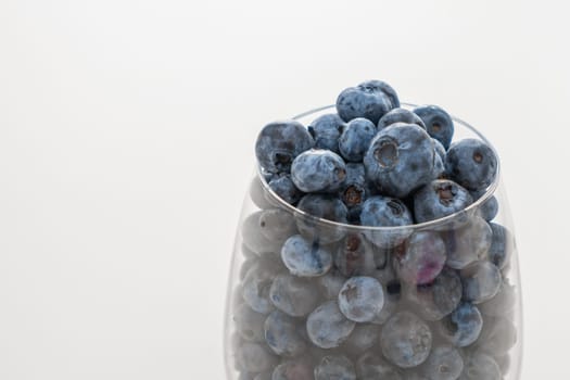 Glass bowl with blueberries on white table, close up.