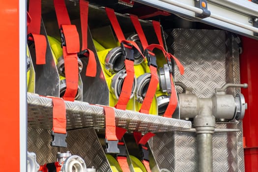 Rolled yellow hoses fastened in cells by belts with clamps in open fire truck metal body at contemporary station close view