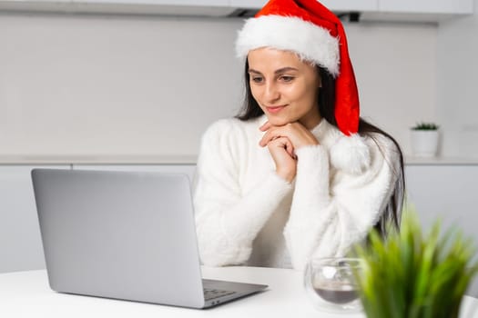 A charming woman in a Santa Claus hat has an online meeting on Christmas holidays at modern home interior.