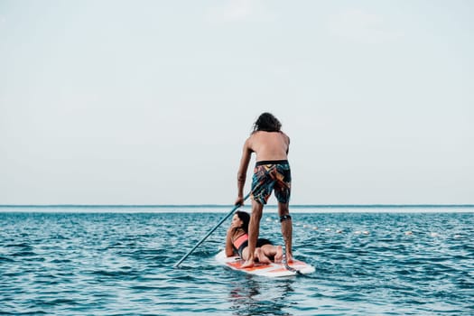 Sea woman and man on sup. Silhouette of happy young woman and man, surfing on SUP board, confident paddling through water surface. Idyllic sunset. Active lifestyle at sea or river