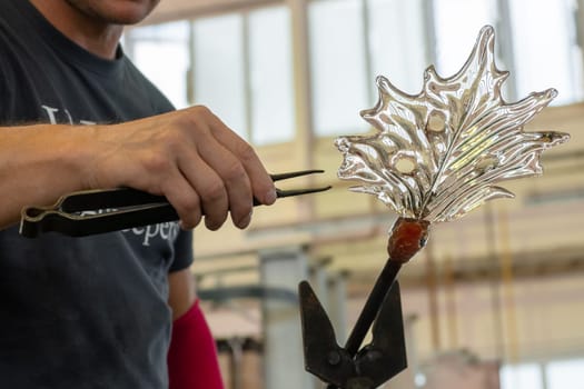 Close up man makes a leaf from the glass for vase or chandelier using tongs and blowpipe.