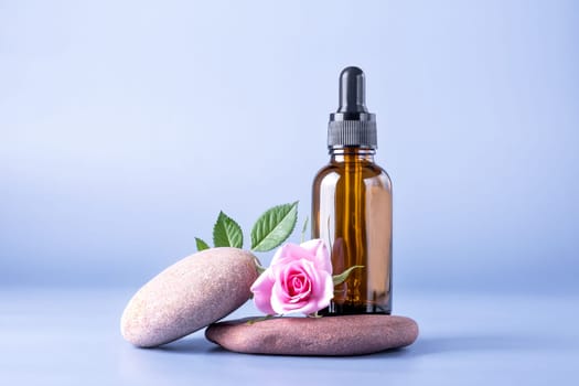 Glass brown bottle with a pipette for a cosmetic product with a rose on stones. Natural cosmetics for face and body skin care. Selective focus.