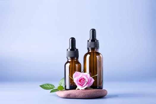 Two glass brown bottles with a pipette for a cosmetic product with a rose on the stones. Natural cosmetics for face and body skin care. Selective focus.