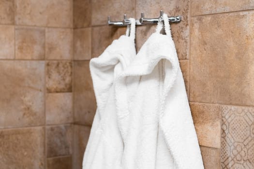 Fresh white bathrobes hanging on hooks in the bathroom in hotel room