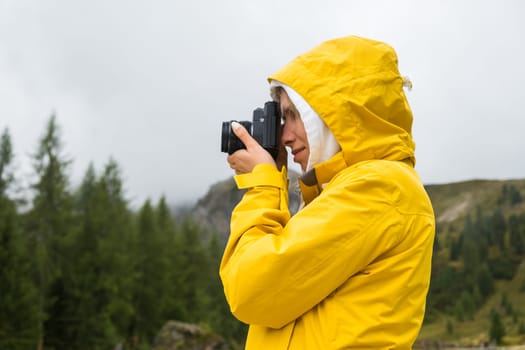 Lady in yellow jacket makes photos of meadows of Alps. Young woman tourist captures moments with camera and explores foggy hillside in mountains
