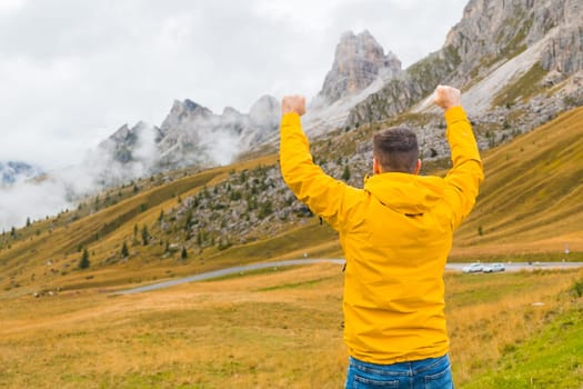 Happy man spreads hands and sees Passo Giau pass in dense fog. Young traveler enjoys standing in Italian Alps