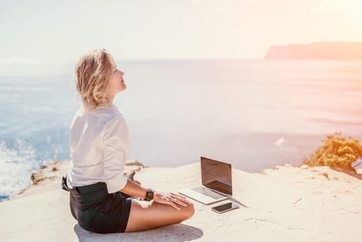 Happy girl doing yoga with laptop working at the beach. beautiful and calm business woman sitting with a laptop in a summer cafe in the lotus position meditating and relaxing. freelance girl remote work beach paradise