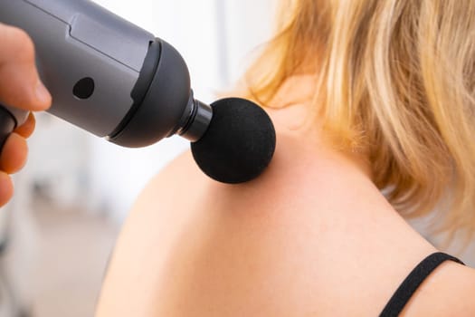 A therapist massaging a womans neck using a massage gun. Physical therapy for recovery.