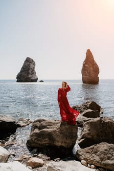 Woman travel sea. Young Happy woman in a long red dress posing on a beach near the sea on background of volcanic rocks, like in Iceland, sharing travel adventure journey