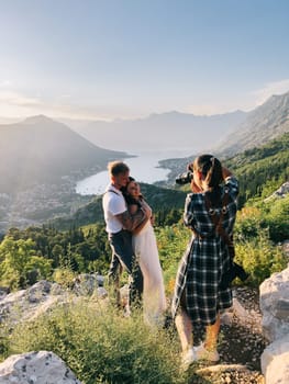 Girl-photographer photographs the embracing bride and groom on a rock above the Kotor Bay. High quality photo