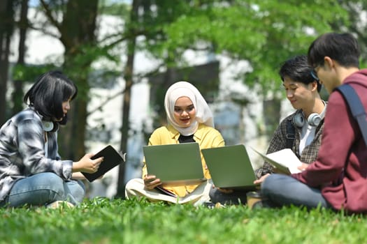 Multicultural students doing group project together on green lawn at university campus. Education, Learning and community.