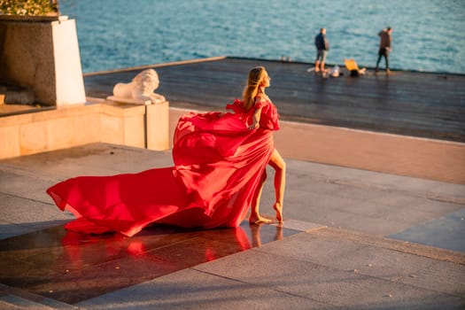 Sunrise red dress. A woman in a long red dress against the backdrop of sunrise, bright golden light of the sun's rays. The concept of femininity, harmony