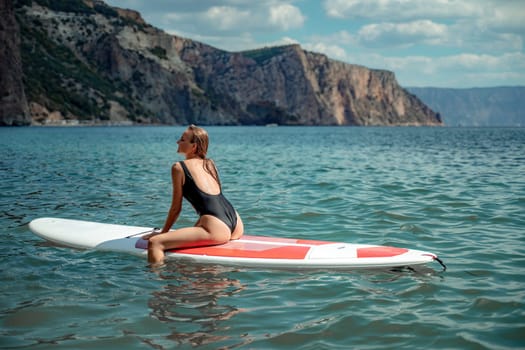 Woman sap sea. Sports girl on a surfboard in the sea on a sunny summer day. In a black bathing suit, he sits on a sapa in the sea. Rest on the sea