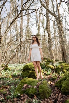 Snowdrops galanthus woman. She stands in a white dress on a meadow with snowdrops in a spring forest.