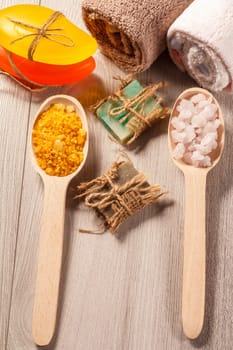 Wooden spoons with yellow and white sea salt and handmade soap for bathroom procedures with towels on the background. Spa products and accessories