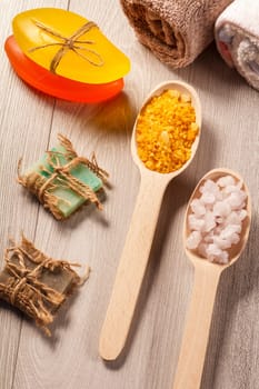 Wooden spoons with yellow and white sea salt and handmade soap for bathroom procedures with towels on the background. Spa products and accessories