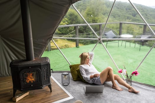 Happy young woman chatting online by using laptop in dome camping. Glamping vacation concept.