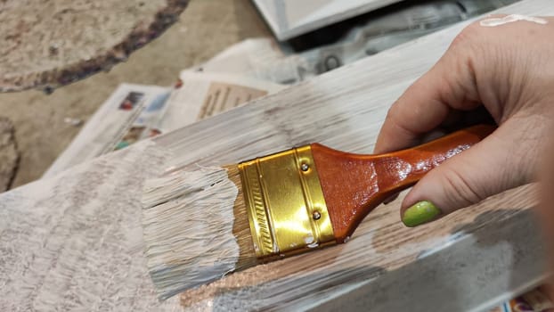 Woman hand painting on wooden boards with Brush full of white paint. Painting of new wood board or furniture and old newspaper on background. Partial focus